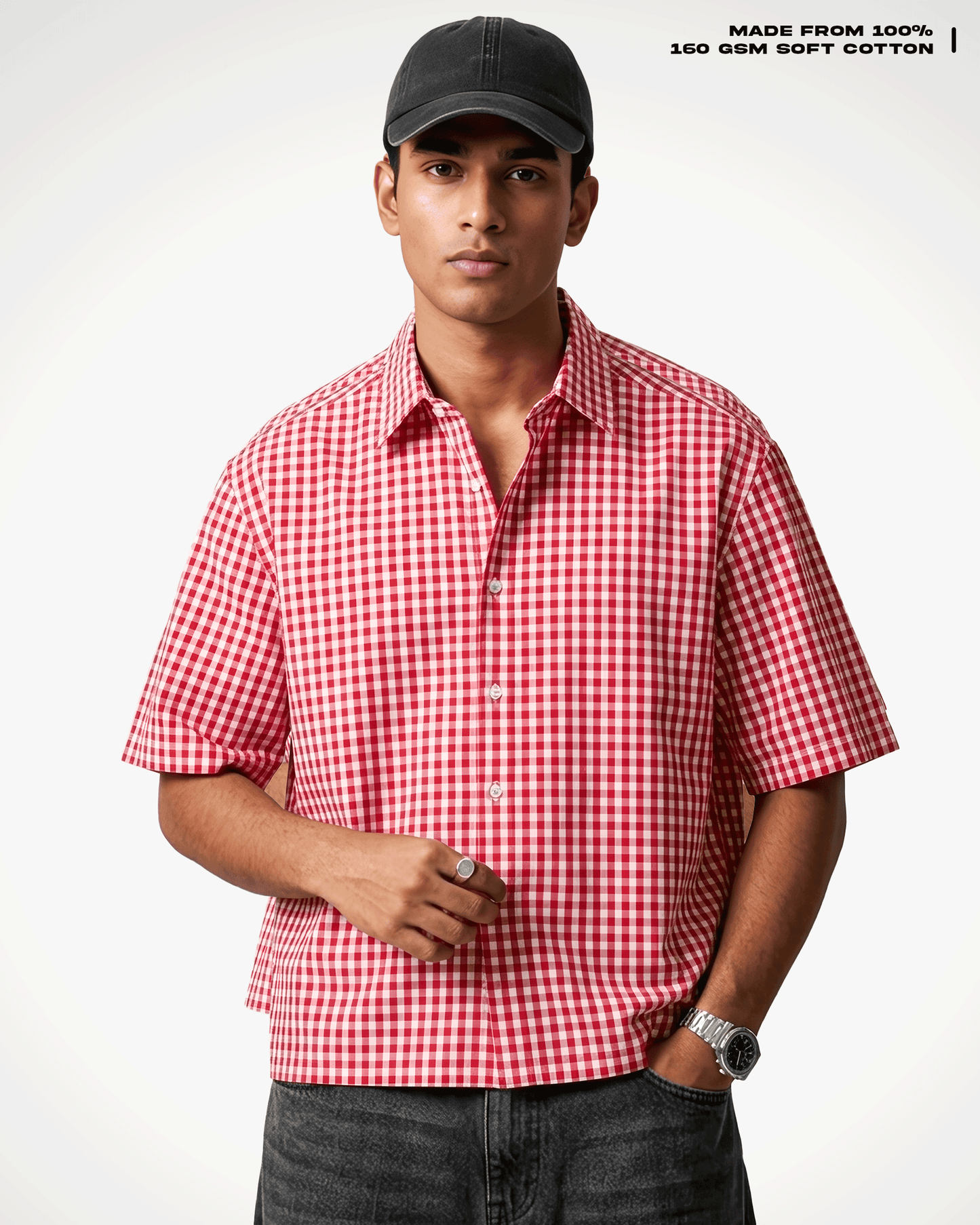 A man wearing a Red Madras Check Shirt boxy fit shirt by Covert, a black baseball cap, and dark gray jeans, standing against a light gray background. Text in the top right corner reads 'MADE FROM 100% 160 GSM SOFT COTTON'.