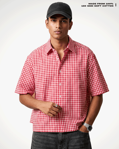 A man wearing a Red Madras Check Shirt boxy fit shirt by Covert, a black baseball cap, and dark gray jeans, standing against a light gray background. Text in the top right corner reads 'MADE FROM 100% 160 GSM SOFT COTTON'.
