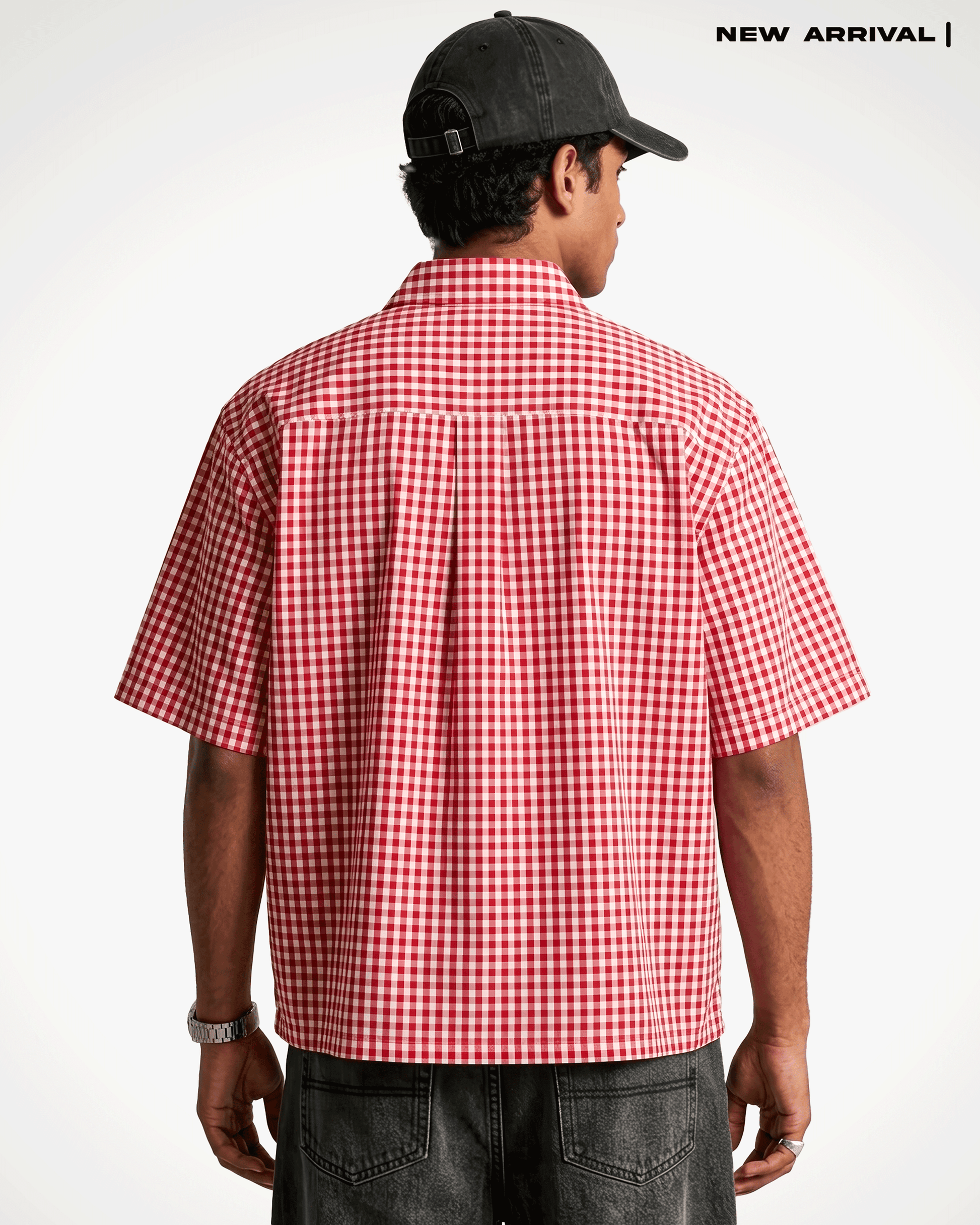 A man viewed from behind wearing a Red Madras Check Shirt boxy fit shirt by Covert, a black baseball cap, and dark gray jeans. The text 'NEW ARRIVAL |' is printed in the top right corner against a clean white background.