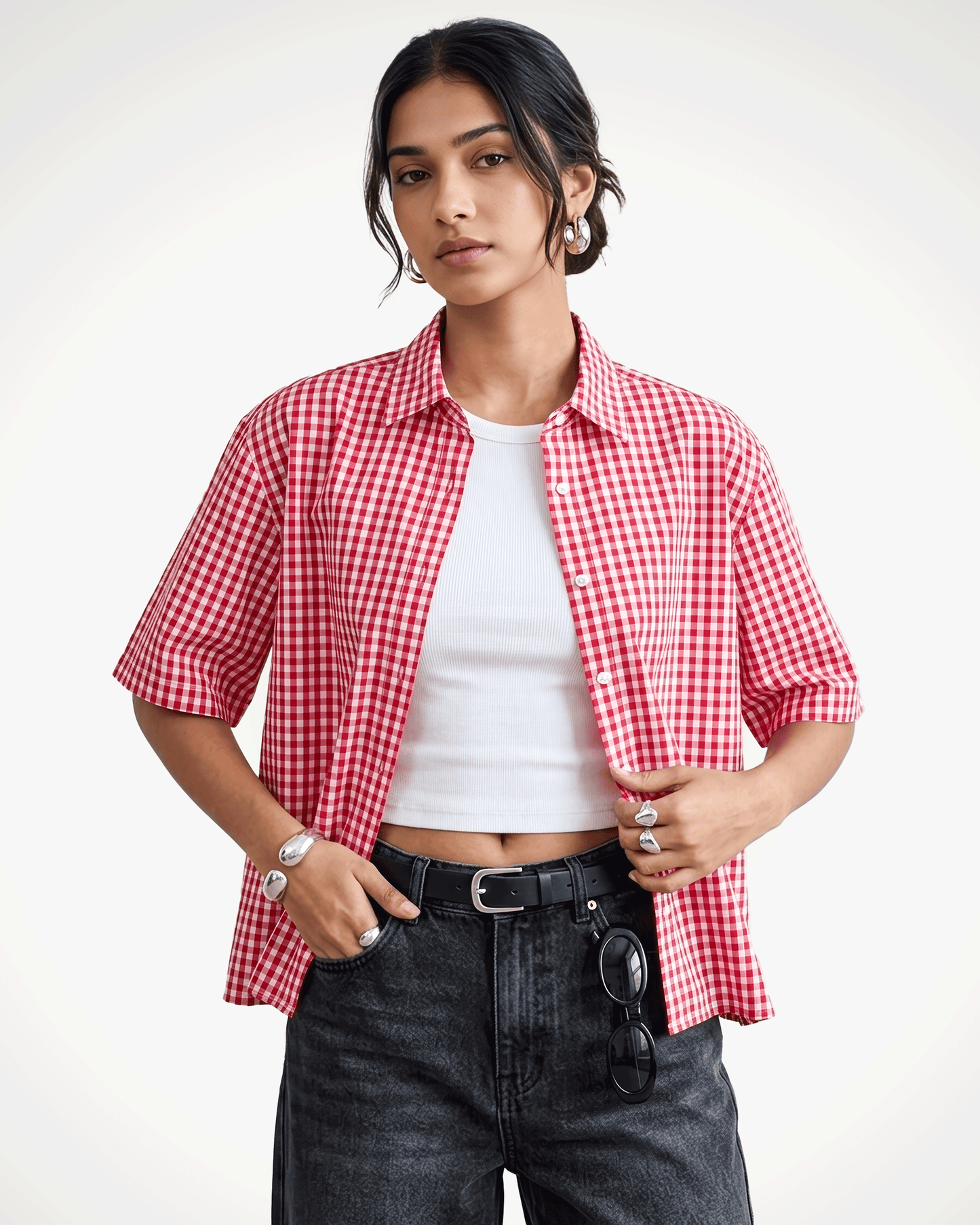 A model wearing Red Madras Check Shirt boxy fit shirt by Covert over a white crop top, paired with dark gray jeans and a black belt, against a plain white studio background.