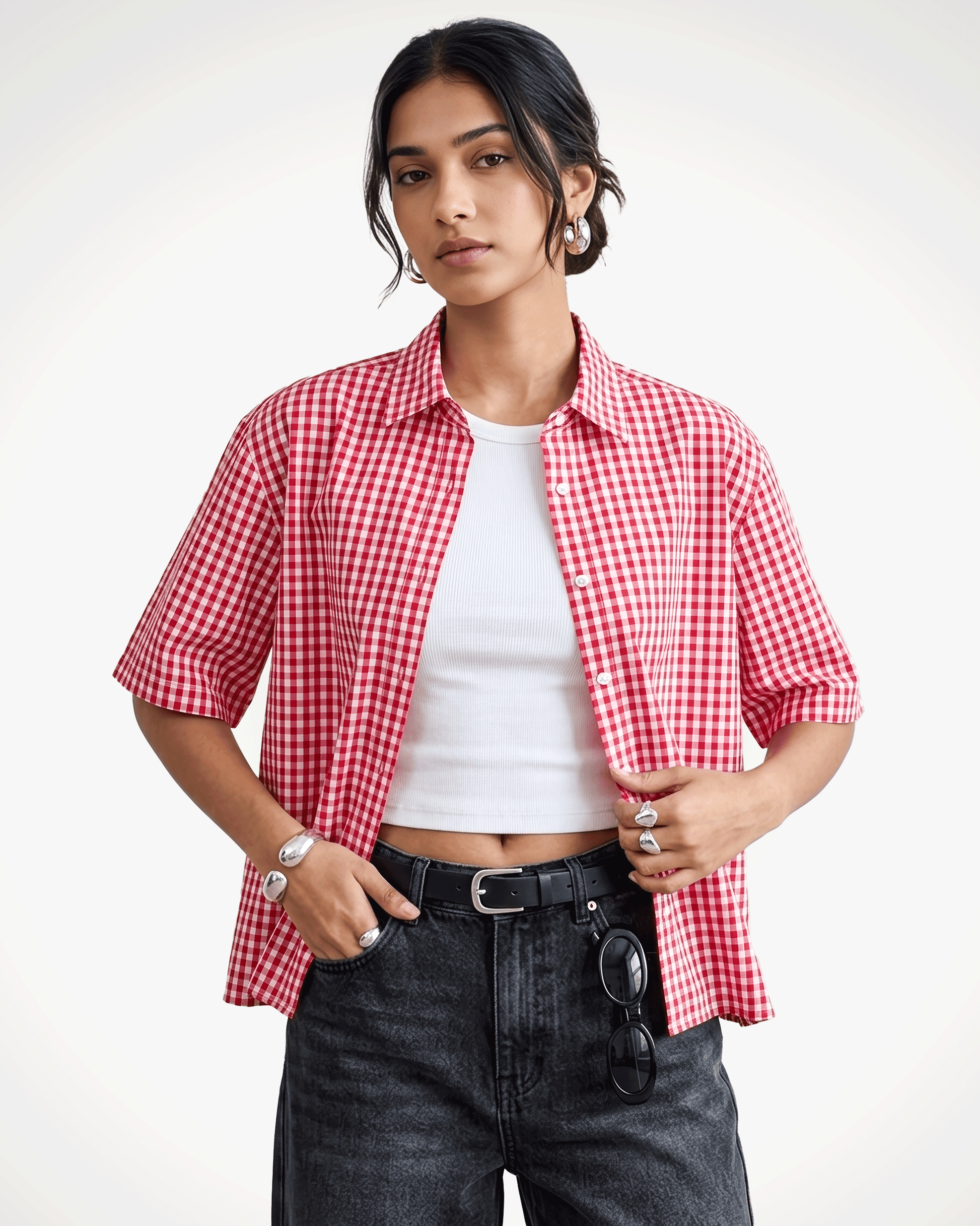 A model wearing Red Madras Check Shirt boxy fit shirt by Covert over a white crop top, paired with dark gray jeans and a black belt, against a plain white studio background.